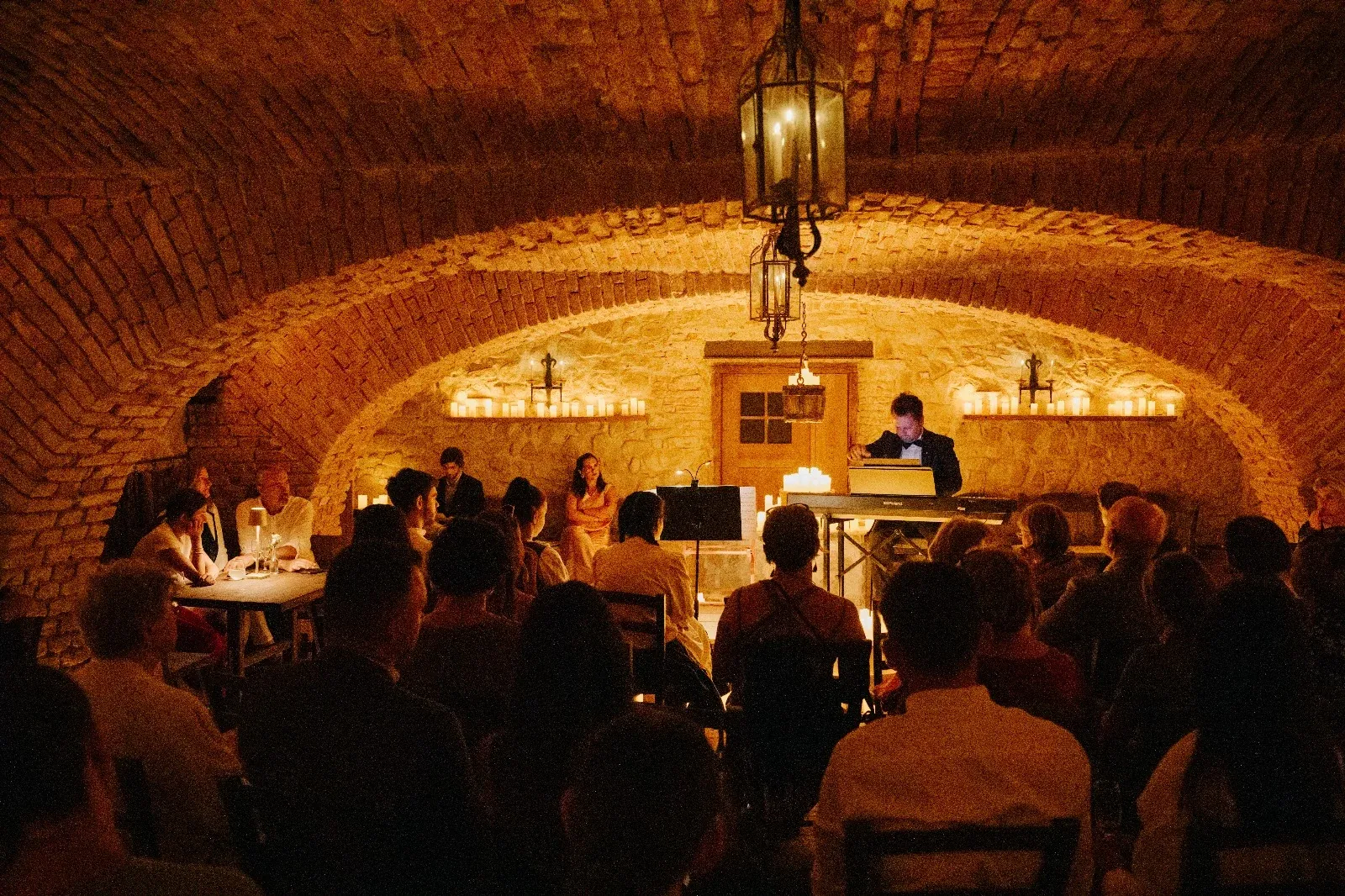 Guests seated at dinner tables watching a concert beneath the brick vaults of the castle wine cellar