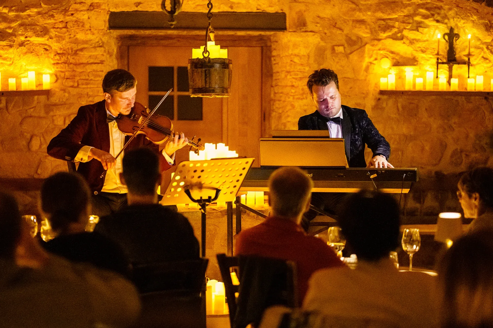 Violinist and pianist performing for guests in the candlelit Kálnoky Castle wine cellar